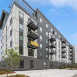 An exterior image of a new five over 1 apartment building with grey walls and brick first floor exterior.